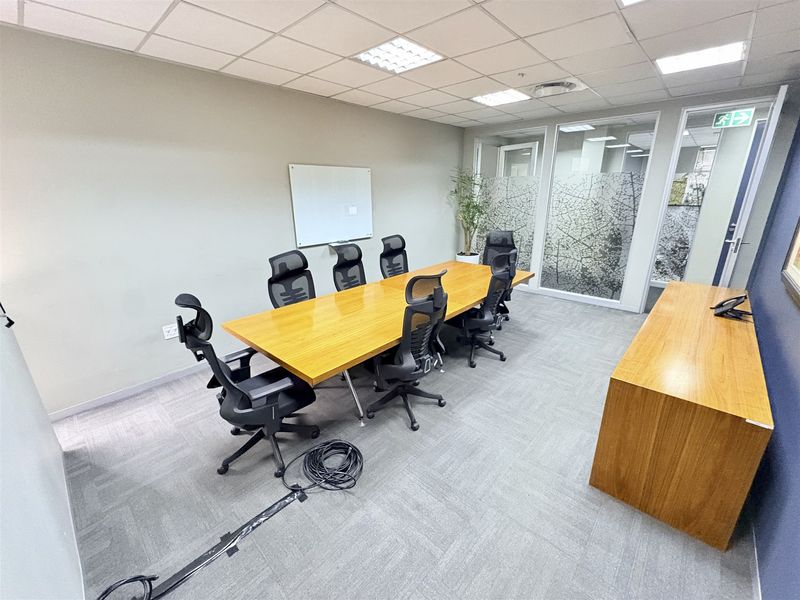 A professional office meeting room featuring a large wooden conference table, glass partition walls with privacy film, and a suspended ceiling with recessed lighting.