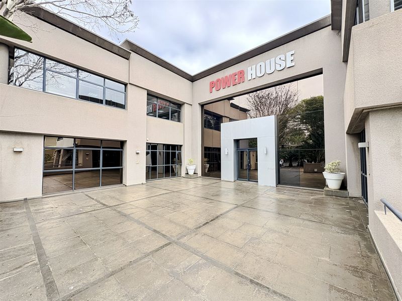 A professional exterior view of the Power House office building entrance, featuring a paved courtyard and modern glass facade.