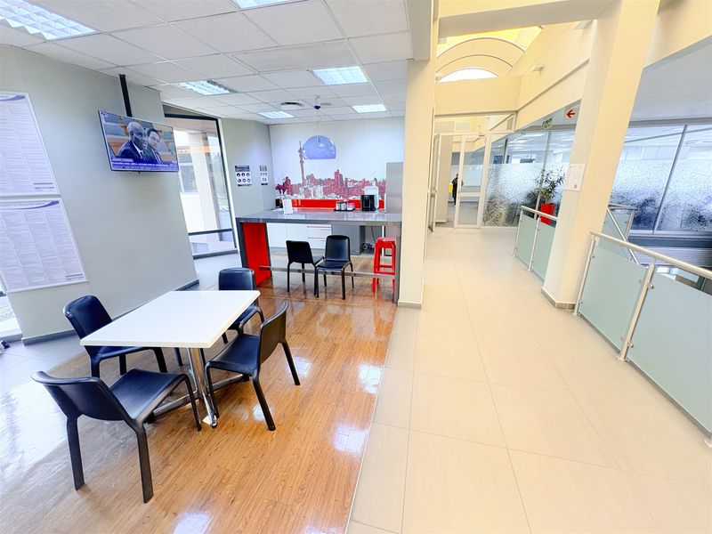 Open-plan office break area featuring a kitchenette counter, mixed flooring, and modern glass balustrades, providing a functional communal space within the office environment.