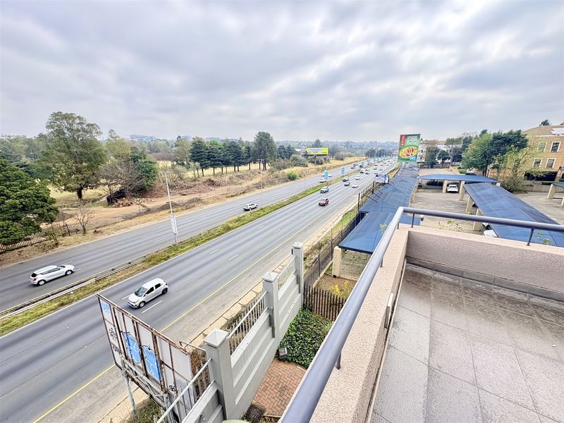 Elevated view from a balcony overlooking a major highway, surrounding landscape, and office parking area with covered carports.