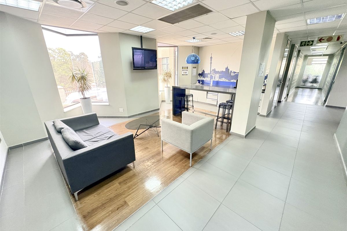 Open-plan office breakout area featuring a kitchenette, wood-look laminate flooring, tiled walkways, and recessed ceiling lighting.
