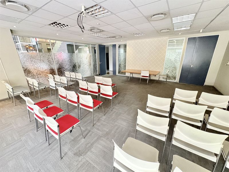 A functional office meeting room featuring suspended ceilings, recessed lighting, carpet tiles, and glass partitioning with decorative privacy film.