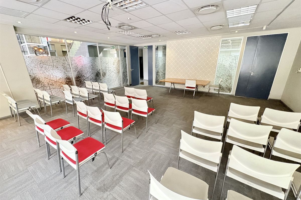 A functional office meeting room featuring suspended ceilings, recessed lighting, carpet tiles, and glass partitioning with decorative privacy film.