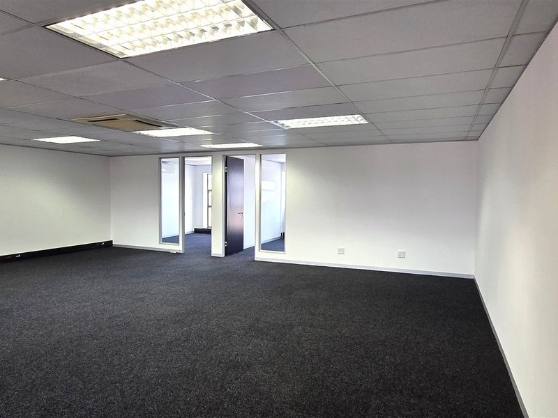 A spacious, open-plan office suite featuring a suspended ceiling with recessed lighting, dark carpeting, and glass-partitioned internal access.