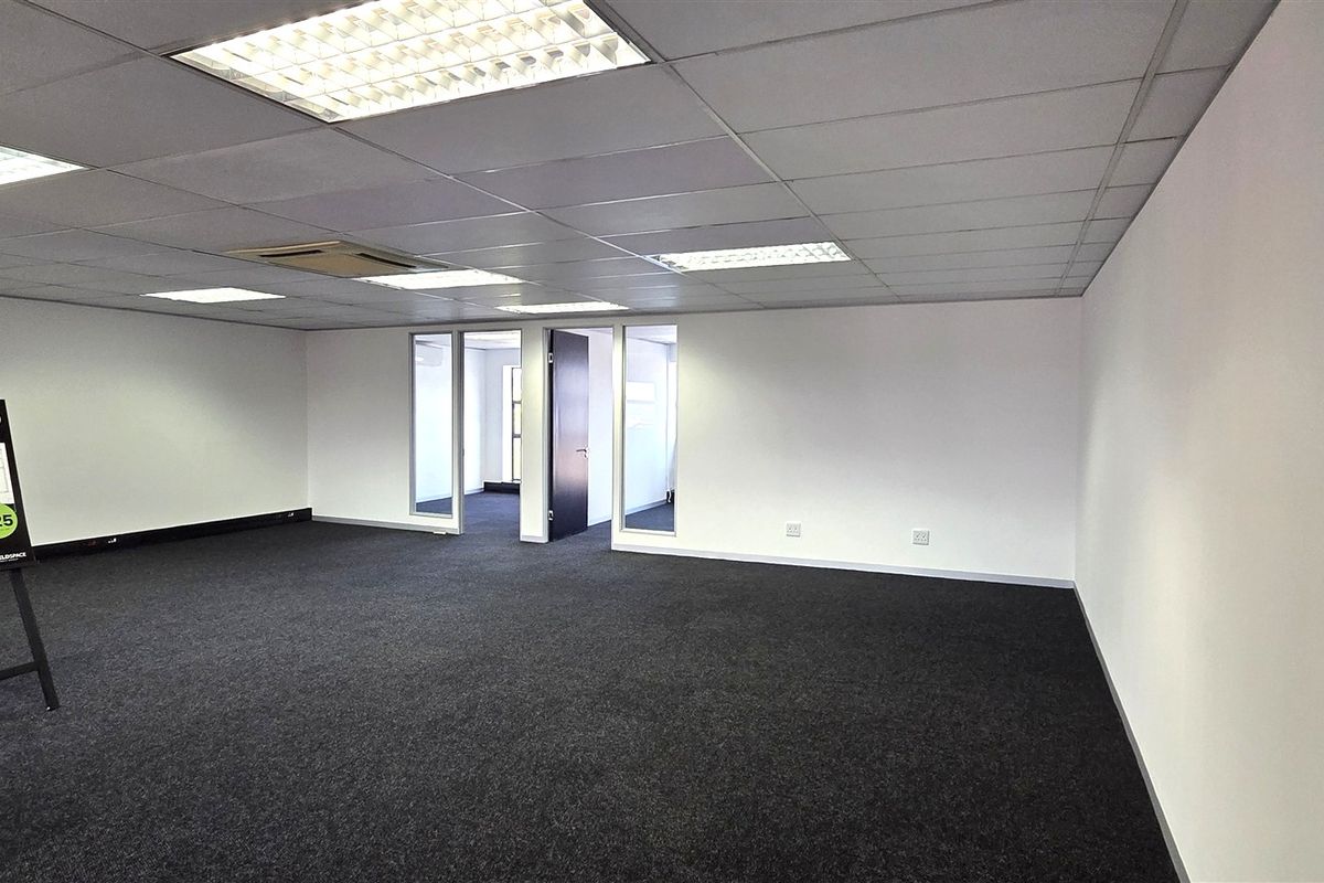 A spacious, open-plan office suite featuring a suspended ceiling with recessed lighting, dark carpeting, and glass-partitioned internal access.