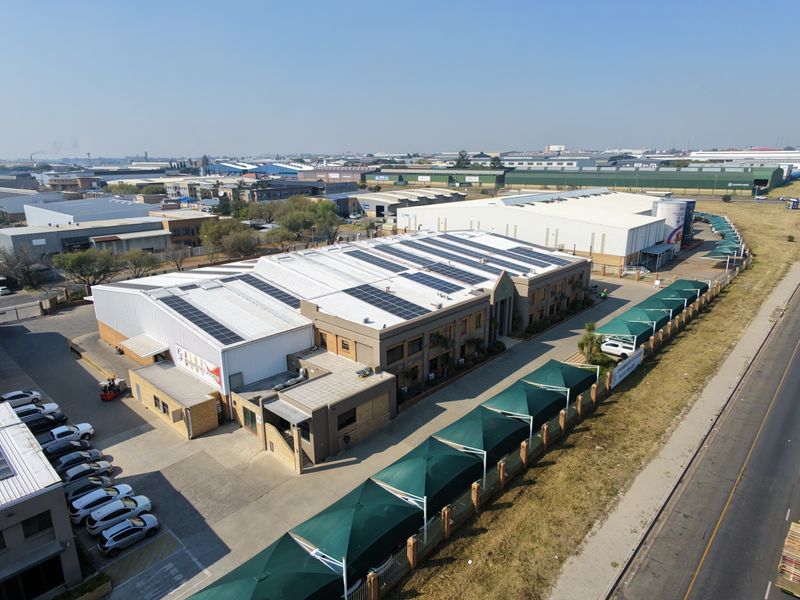 Aerial view of an industrial property featuring a large warehouse with solar panels, paved parking, and shaded parking bays.