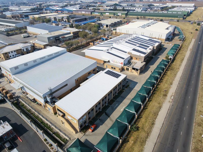Aerial view of an industrial property complex featuring multiple warehouse buildings, solar panel installations, and a paved parking area with shade cloth structures.