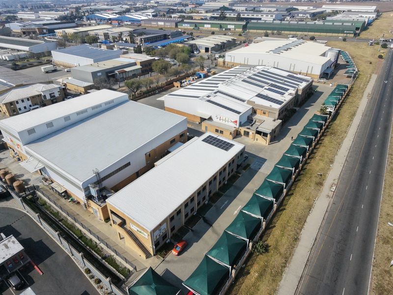 Aerial view of an industrial property complex featuring multiple warehouse buildings, solar panel installations, paved parking areas, and shade cloth carports.