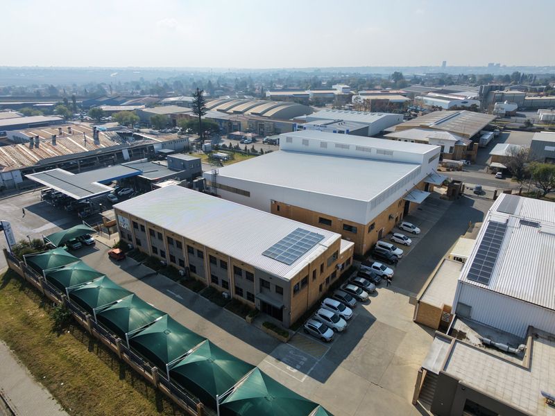 Aerial view of an industrial property complex featuring multiple warehouse buildings, solar panel installations, paved parking areas, and shade cloth carports.