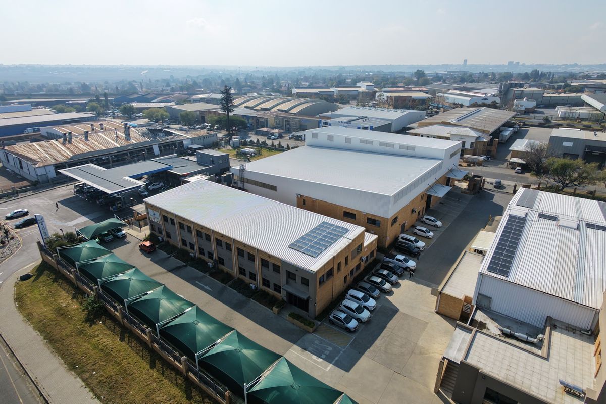 Aerial view of an industrial property complex featuring multiple warehouse buildings, solar panel installations, paved parking areas, and shade cloth carports.
