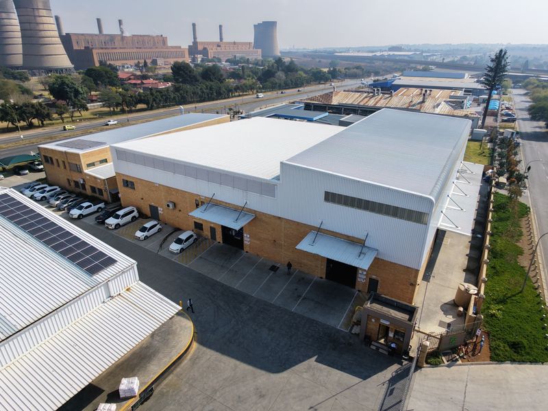 Aerial view of an industrial property featuring large warehouse structures, loading bays, paved parking, and solar panel installations.