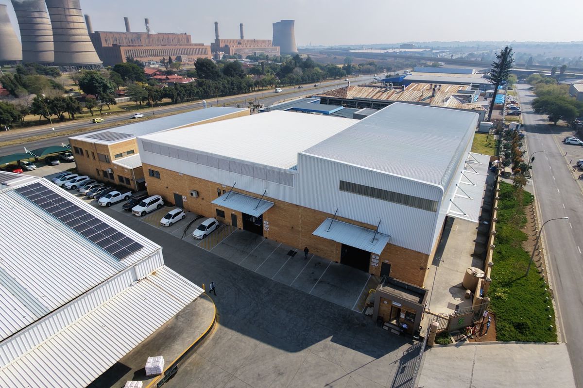 Aerial view of an industrial property featuring large warehouse structures, loading bays, paved parking, and solar panel installations.