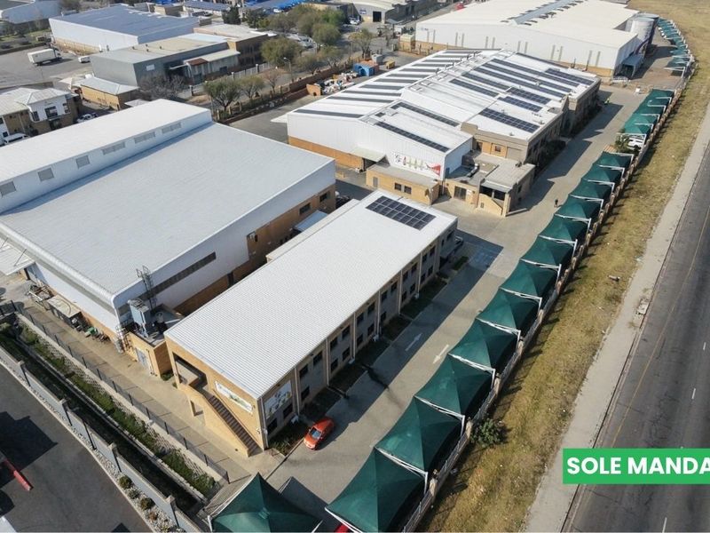Aerial view of an industrial property complex featuring multiple warehouse buildings, solar panel installations, and extensive shaded parking facilities.