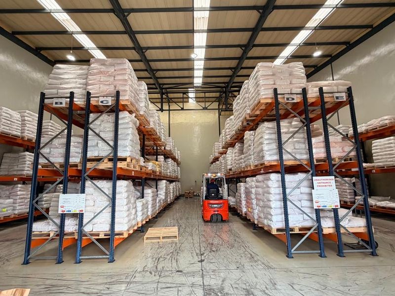 Spacious industrial warehouse featuring high-bay lighting, steel roof trusses with translucent panels, and extensive heavy-duty racking systems for efficient storage.