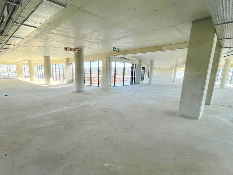 Spacious open-plan office area featuring exposed concrete ceilings, structural columns, and expansive floor-to-ceiling windows providing ample natural light.
