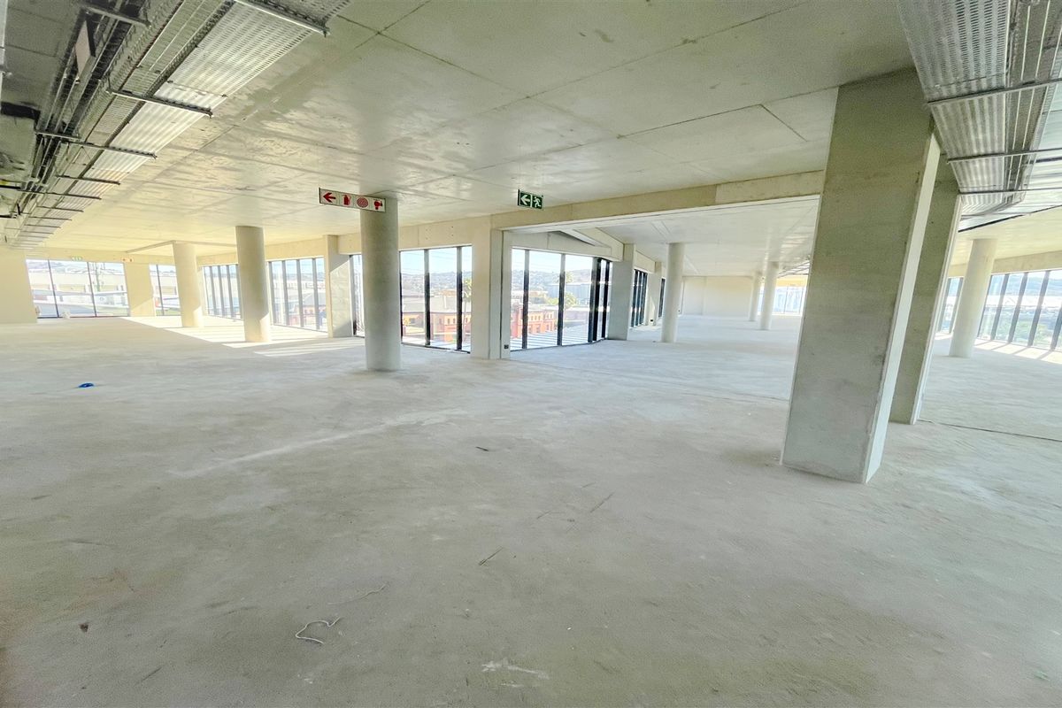 Spacious open-plan office area featuring exposed concrete ceilings, structural columns, and expansive floor-to-ceiling windows providing ample natural light.