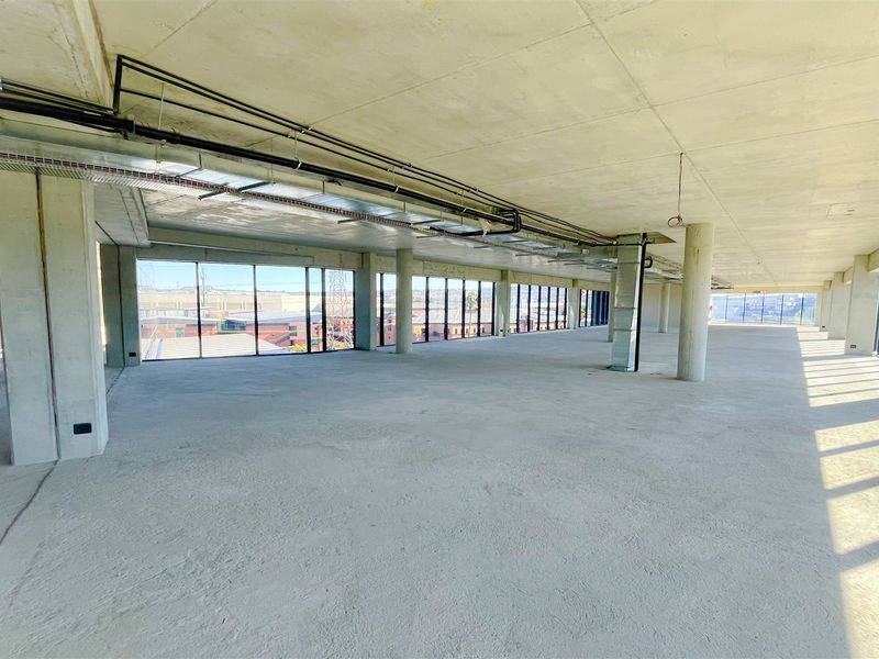 A spacious, open-plan office area featuring exposed concrete ceilings, structural columns, and expansive floor-to-ceiling windows providing ample natural light.