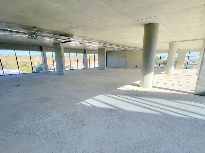 A spacious, open-plan office shell featuring exposed concrete ceilings, structural columns, and expansive floor-to-ceiling windows offering natural light and panoramic views.
