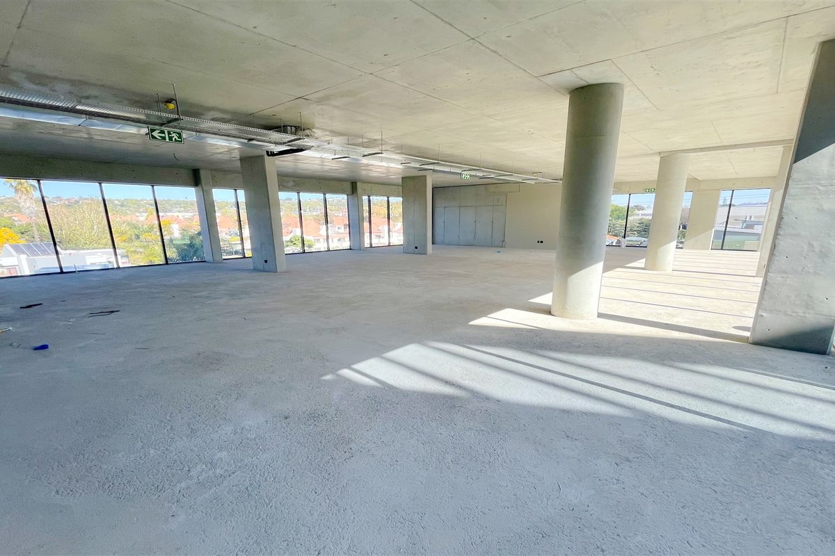 A spacious, open-plan office shell featuring exposed concrete ceilings, structural columns, and expansive floor-to-ceiling windows offering natural light and panoramic views.