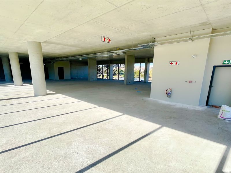 A spacious, open-plan office shell featuring exposed concrete ceilings, structural columns, and essential fire safety infrastructure, ready for custom fit-out.