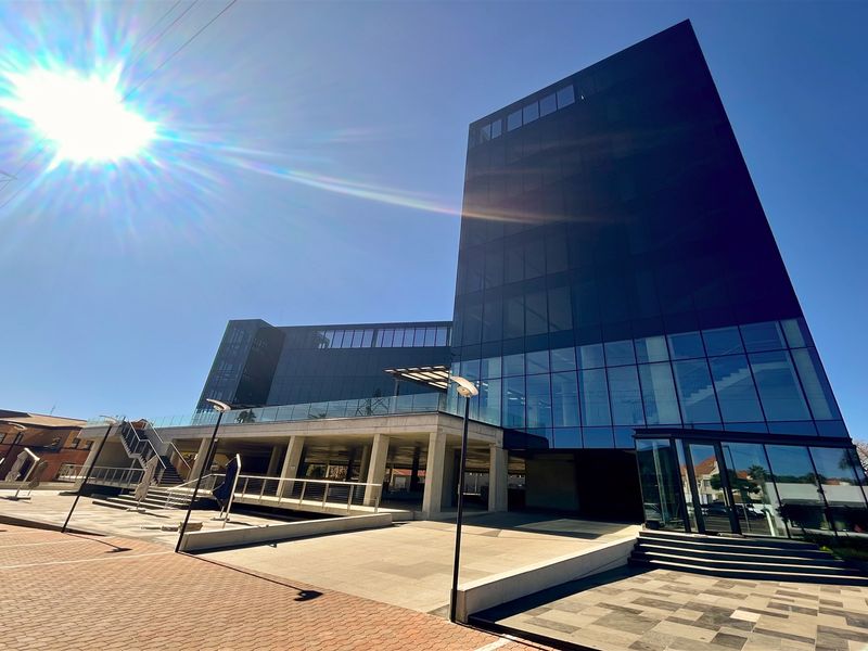Modern multi-story office building featuring a striking glass facade, concrete structural elements, and a paved entrance area.