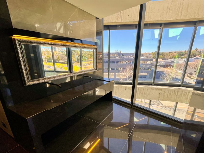 Modern bathroom featuring a sleek double vanity with stone countertop, wall-mounted faucets, and expansive floor-to-ceiling windows offering an urban view.