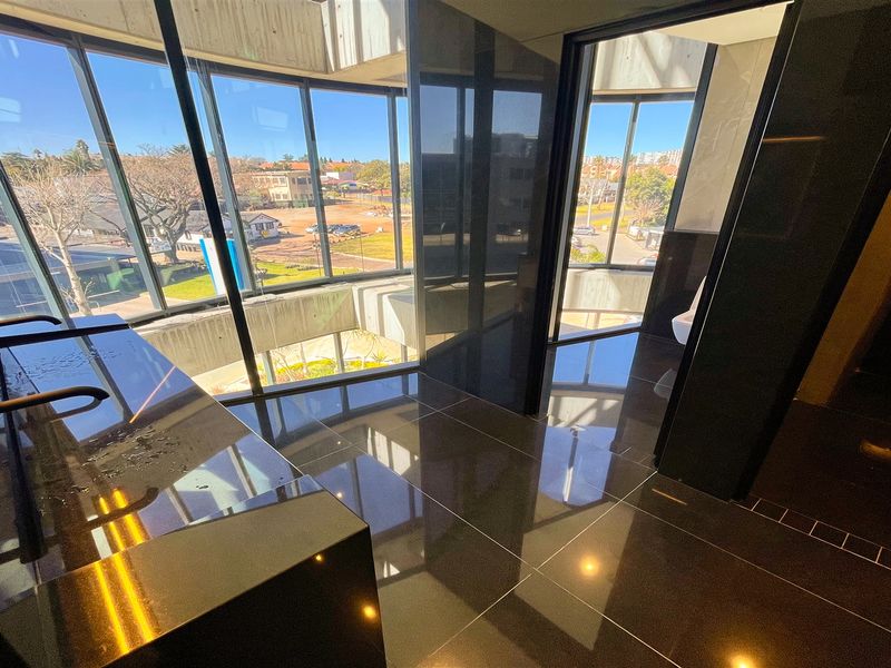 Modern office bathroom featuring high-end finishes, floor-to-ceiling windows with natural light, sleek vanity, and contemporary wall-mounted toilet.