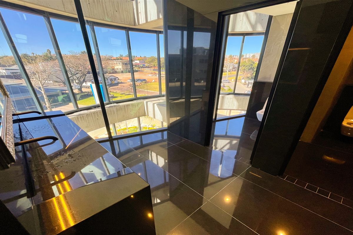 Modern office bathroom featuring high-end finishes, floor-to-ceiling windows with natural light, sleek vanity, and contemporary wall-mounted toilet.