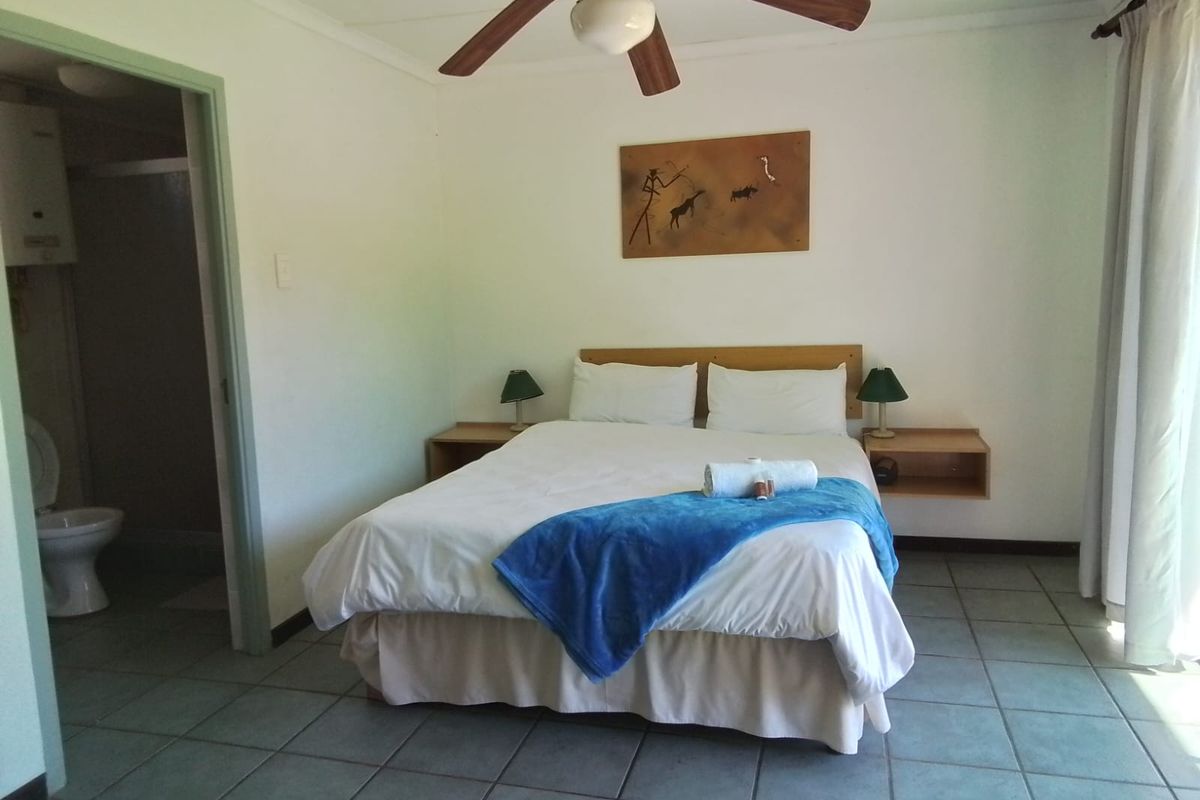 A functional bedroom featuring tiled flooring, a ceiling fan, and direct access to an en-suite bathroom with built-in bedside shelving.