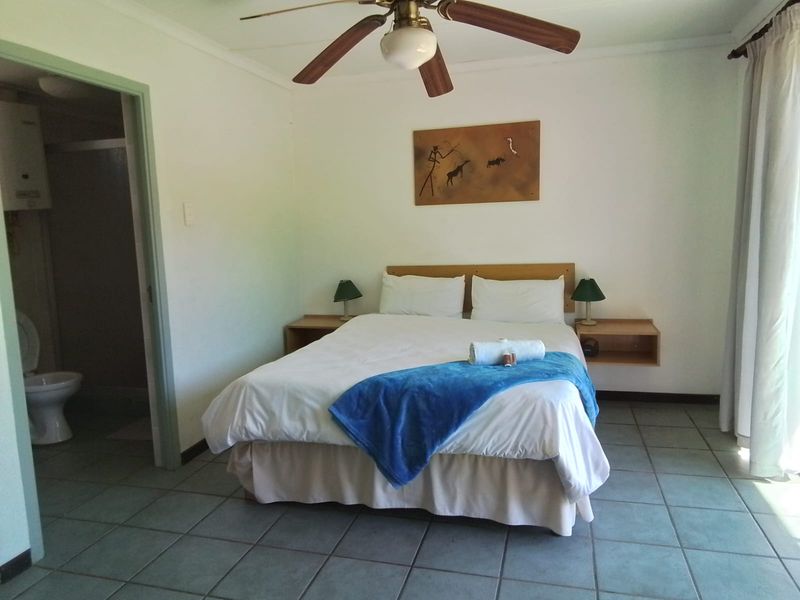 A functional bedroom featuring tiled flooring, a ceiling fan, and direct access to an en-suite bathroom with built-in bedside shelving.