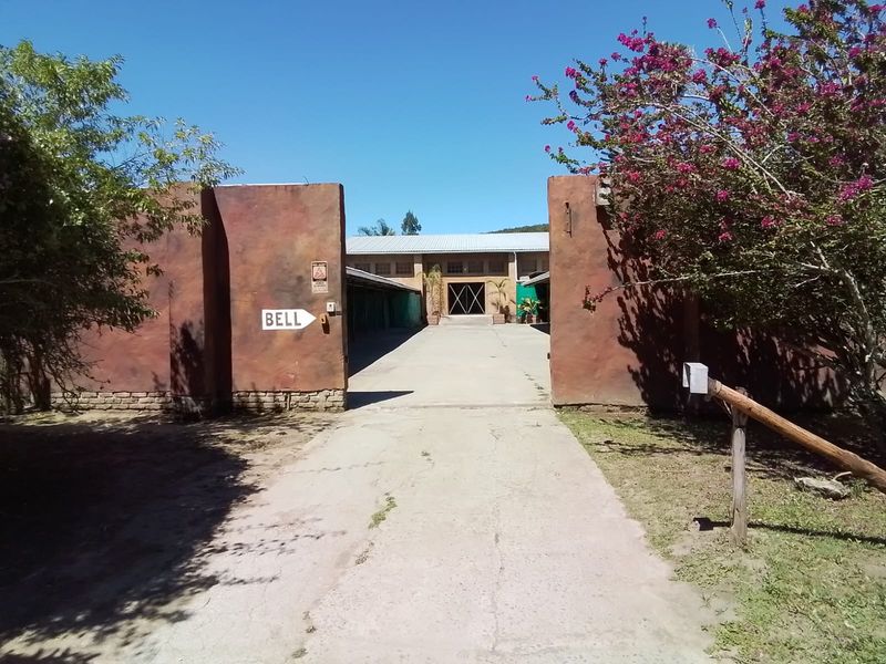 Entrance view of the farm property featuring a concrete driveway leading to a main building with a corrugated metal roof and boundary walls.