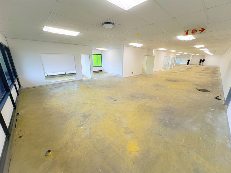 Spacious open-plan office area featuring a suspended ceiling, recessed lighting, and large windows, currently awaiting new flooring installation.