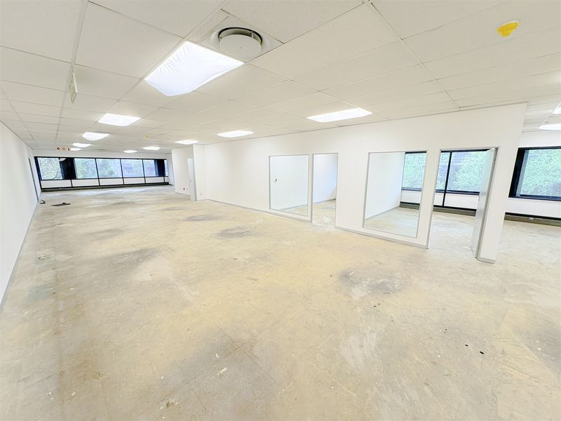 A spacious, open-plan office area featuring large windows, internal glass partitions, and a suspended ceiling, currently in a vacant, shell-like condition.