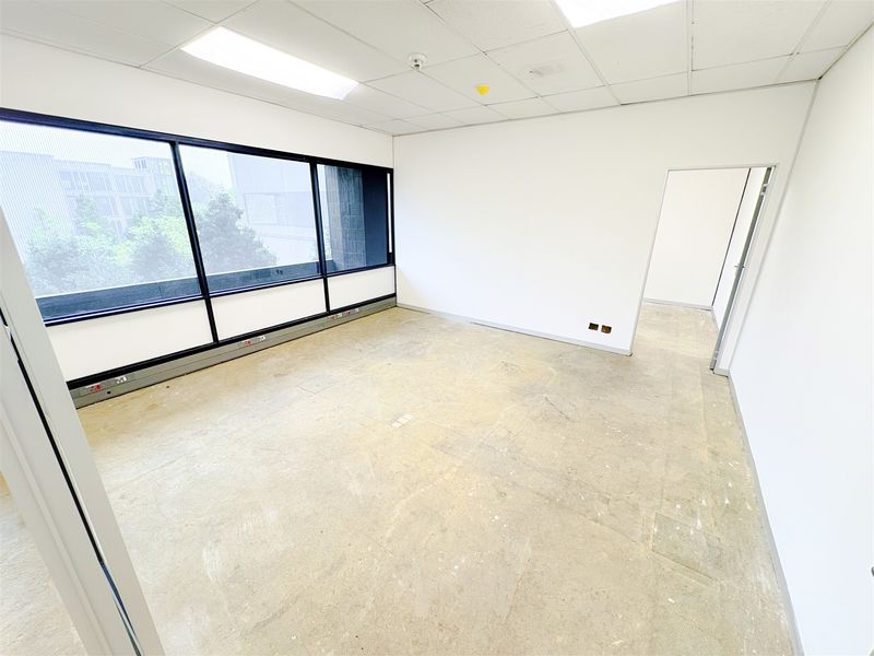 An empty, open-plan office space featuring large windows, suspended ceilings with recessed lighting, and perimeter trunking for power and data connectivity.