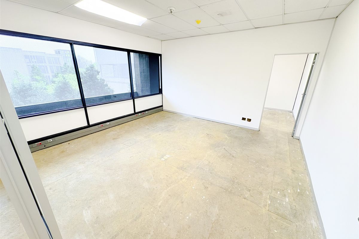 An empty, open-plan office space featuring large windows, suspended ceilings with recessed lighting, and perimeter trunking for power and data connectivity.