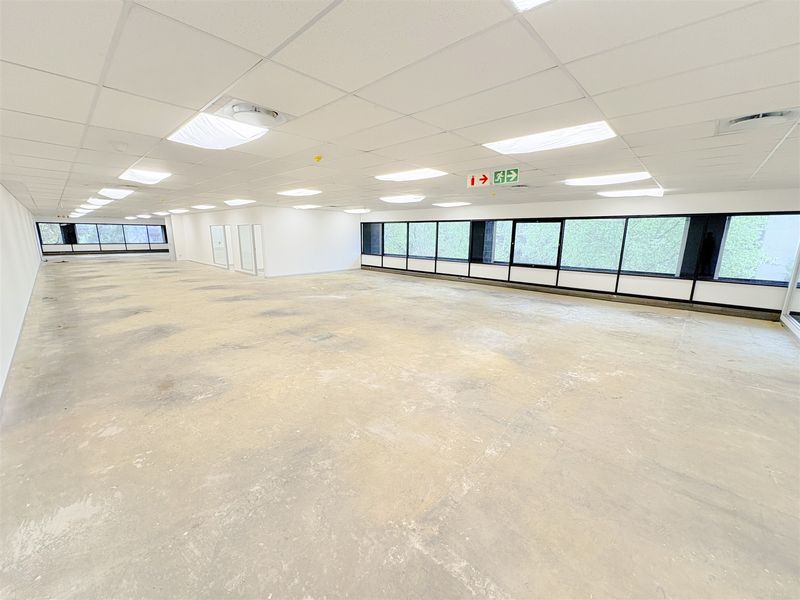A large, open-plan office space featuring a suspended ceiling, recessed lighting, and expansive windows, currently awaiting floor finishing.