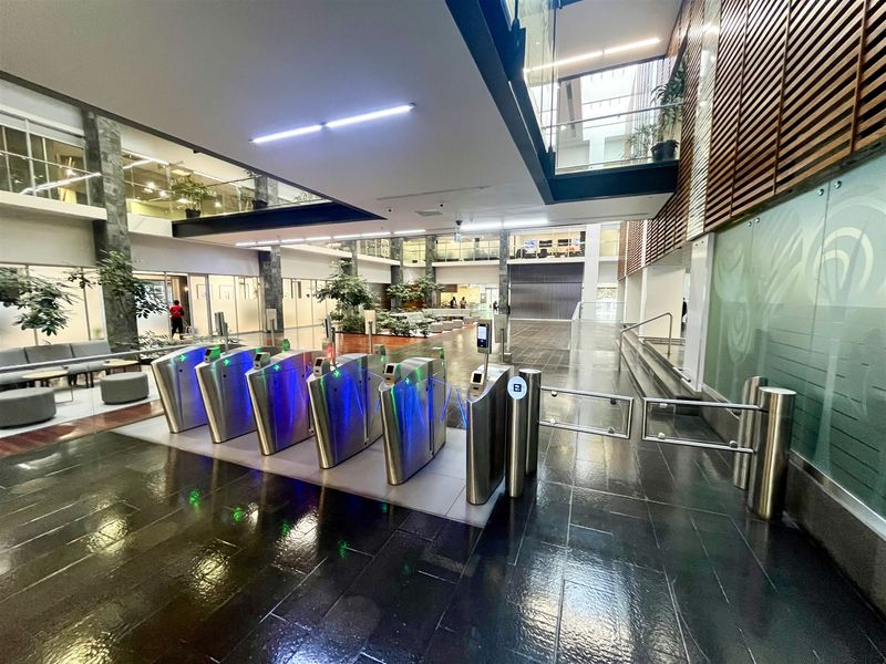 Modern office building lobby featuring high-end security turnstiles, polished stone flooring, and contemporary architectural finishes with glass and timber elements.