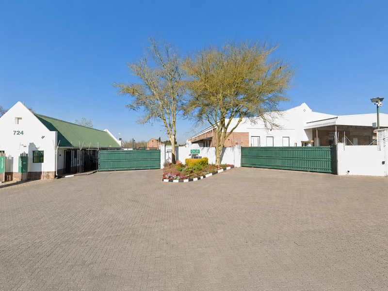 Front entrance view of the industrial property featuring a paved driveway, secure gated access, perimeter walling with electric fencing, and professional signage.