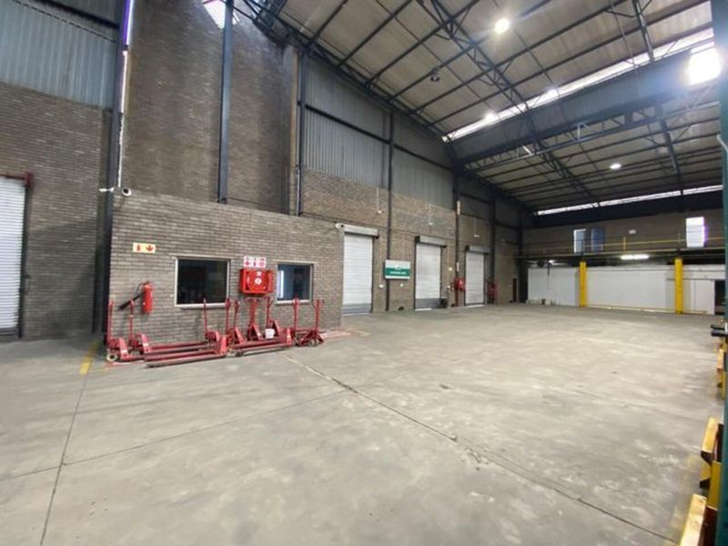 Spacious industrial warehouse featuring high ceilings with exposed steel trusses, concrete flooring, and multiple roller shutter doors for efficient loading and access.