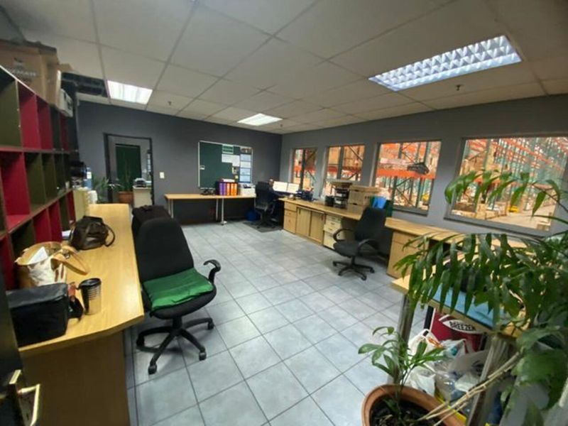 Functional industrial office space featuring tiled flooring, built-in desk cabinetry, and large windows providing a direct view into the warehouse area.