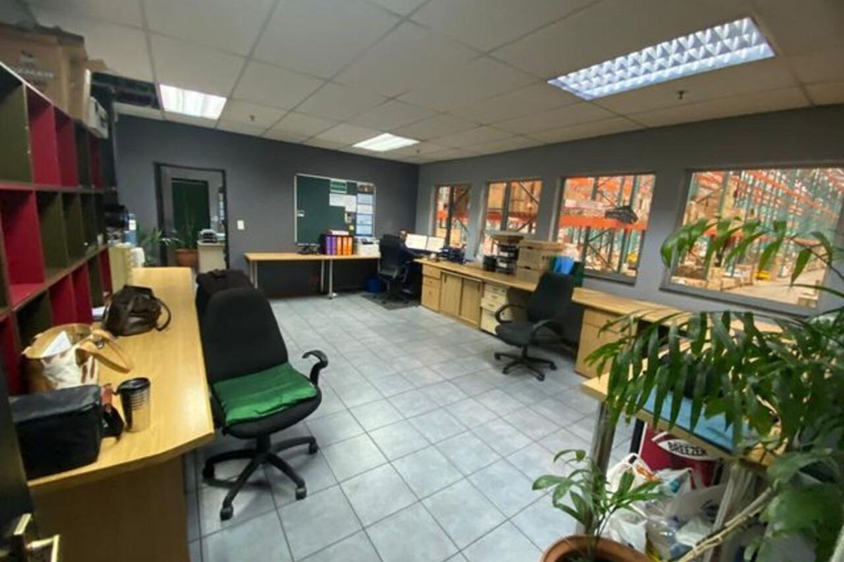 Functional industrial office space featuring tiled flooring, built-in desk cabinetry, and large windows providing a direct view into the warehouse area.