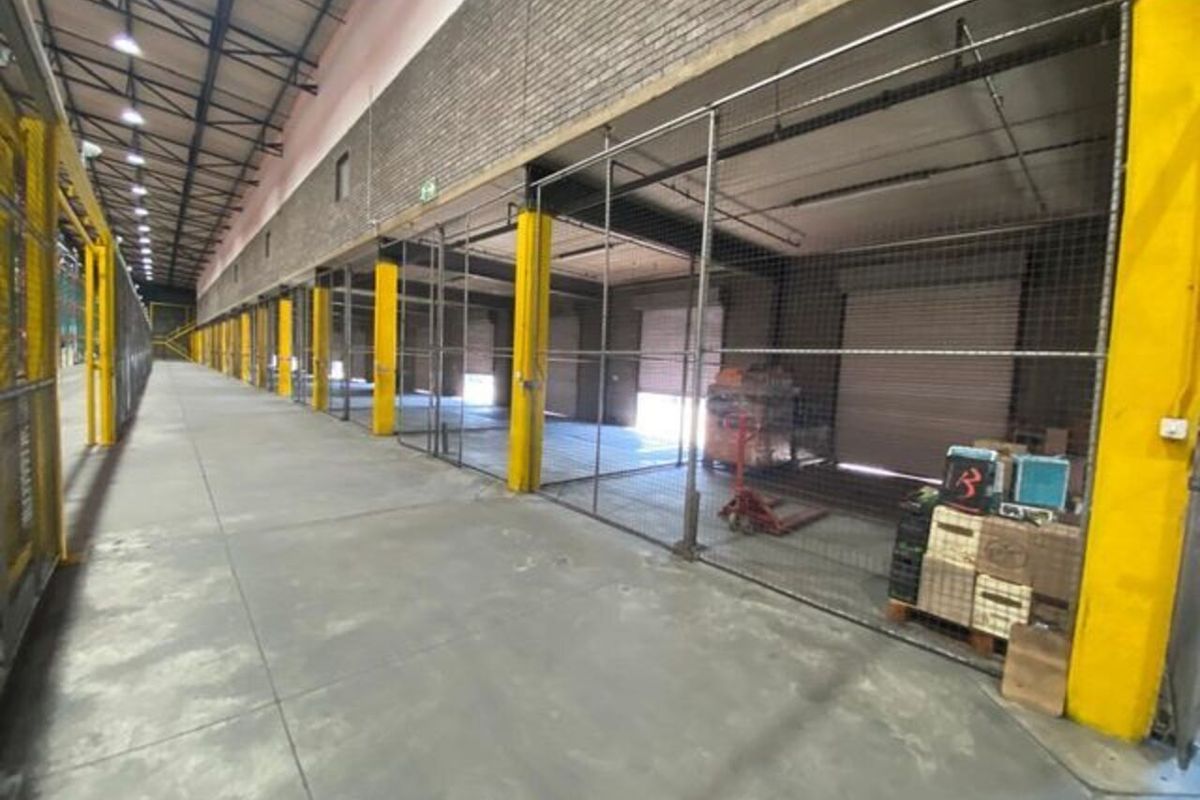 Spacious industrial warehouse area featuring concrete flooring, steel mesh partitioning, and multiple roller shutter doors for efficient loading and storage access.
