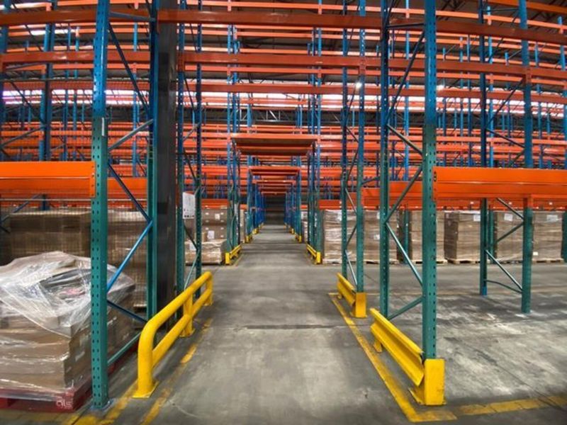 Spacious industrial warehouse interior featuring extensive high-bay pallet racking systems, concrete flooring, and protective steel safety bollards for operational efficiency.