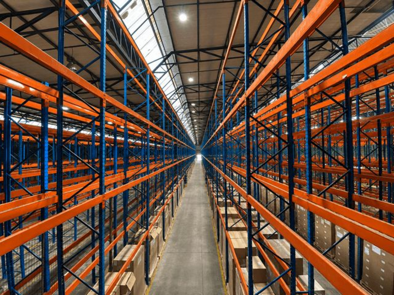 Spacious industrial warehouse interior featuring high-density steel racking systems, concrete flooring, and a high-clearance truss roof with integrated skylights.