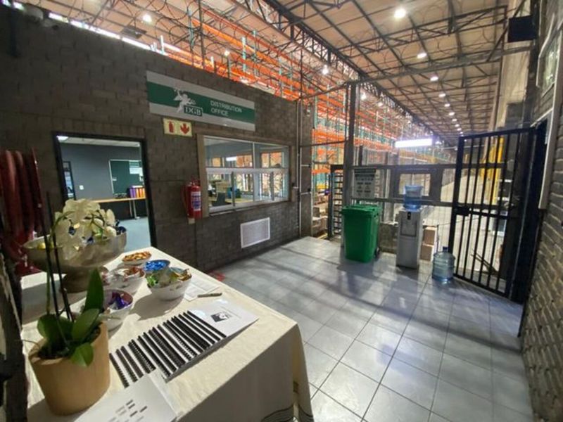 Industrial warehouse interior featuring high-clearance steel roof trusses, heavy-duty racking systems, tiled flooring, and an integrated distribution office partition.