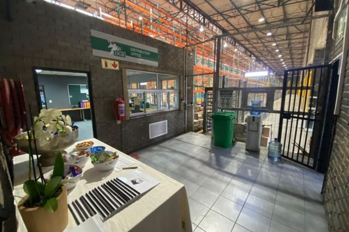 Industrial warehouse interior featuring high-clearance steel roof trusses, heavy-duty racking systems, tiled flooring, and an integrated distribution office partition.