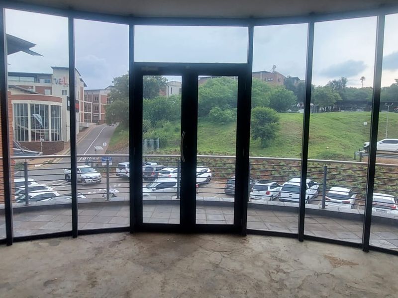 Empty office space featuring floor-to-ceiling windows, double glass doors, and access to a private balcony with metal railings overlooking the parking area.