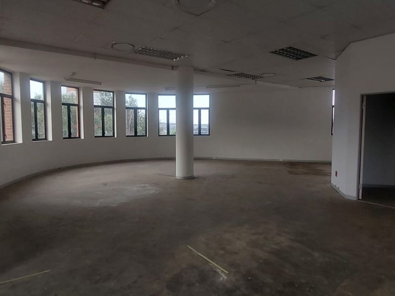 An expansive, vacant open-plan office space featuring a curved wall with large windows, a central structural column, and a suspended ceiling.