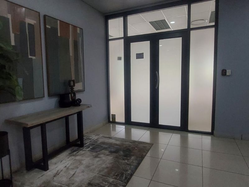 A professional office entry area featuring tiled flooring, a suspended ceiling with recessed lighting, and modern frosted glass double doors.