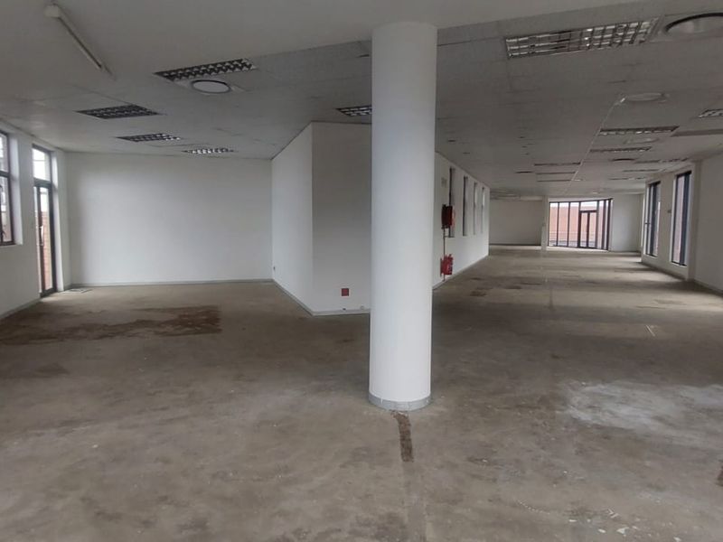 Spacious open-plan office area featuring large windows, a central structural column, and suspended ceiling tiles, ready for custom fit-out.